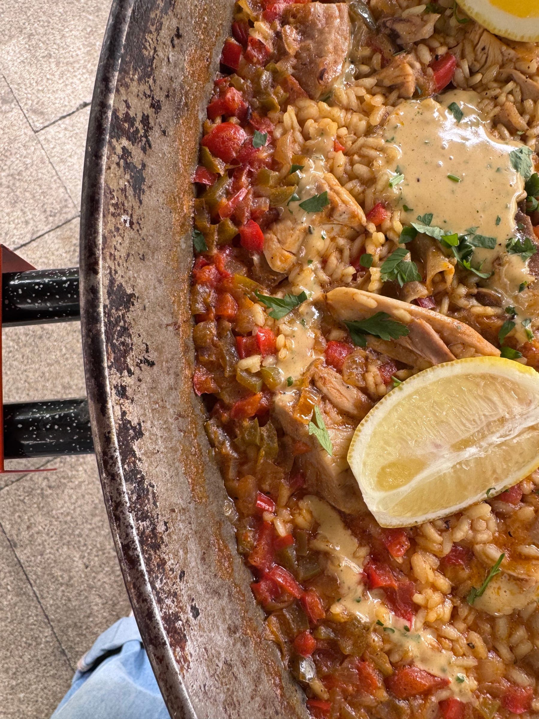 Paella in der Pfanne mit Huhn, Paprika, Petersilie und Zitronenspalten