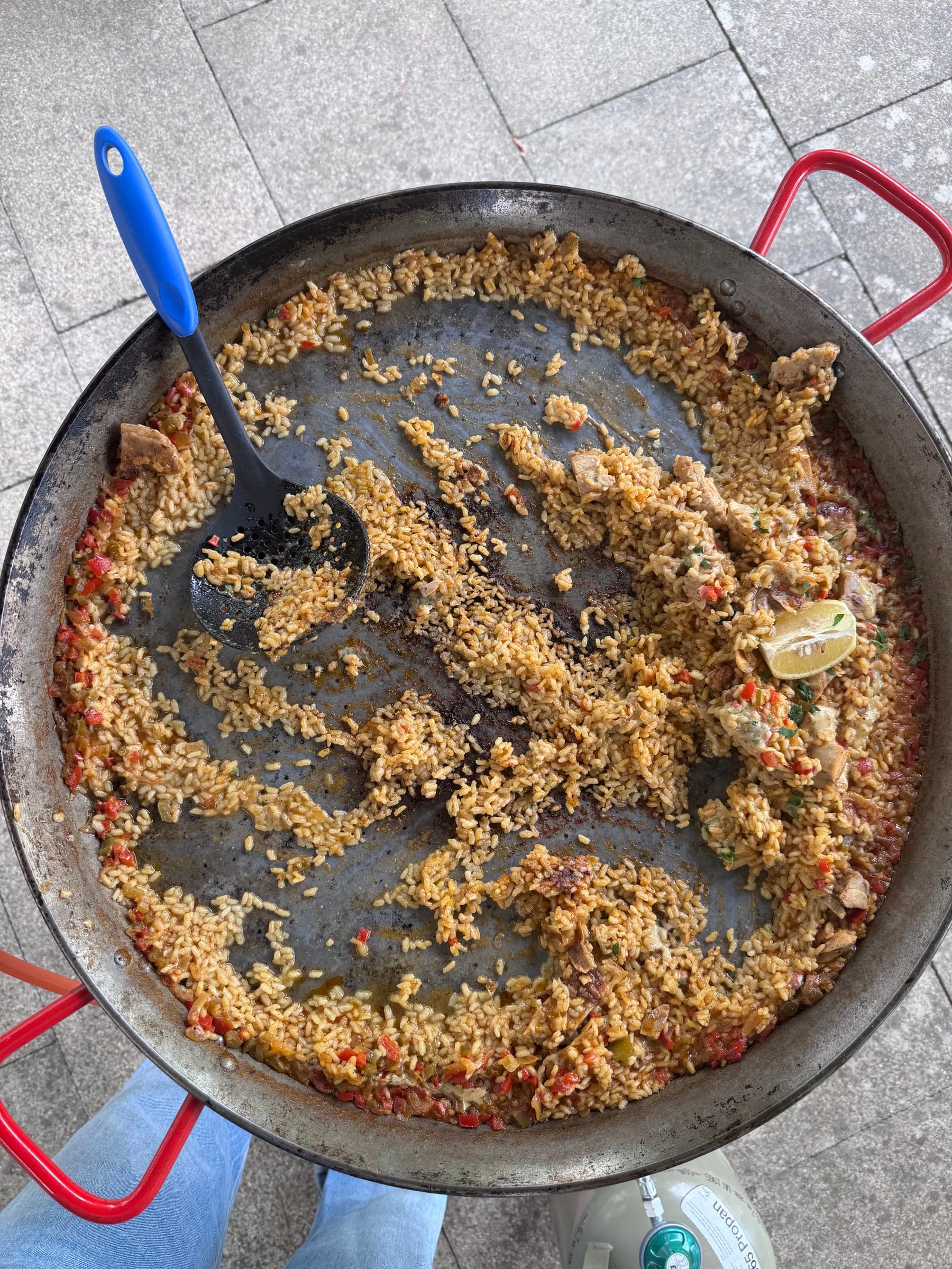 Paellapfanne von oben mit Socarrat, Kelle und Zitronenspalte