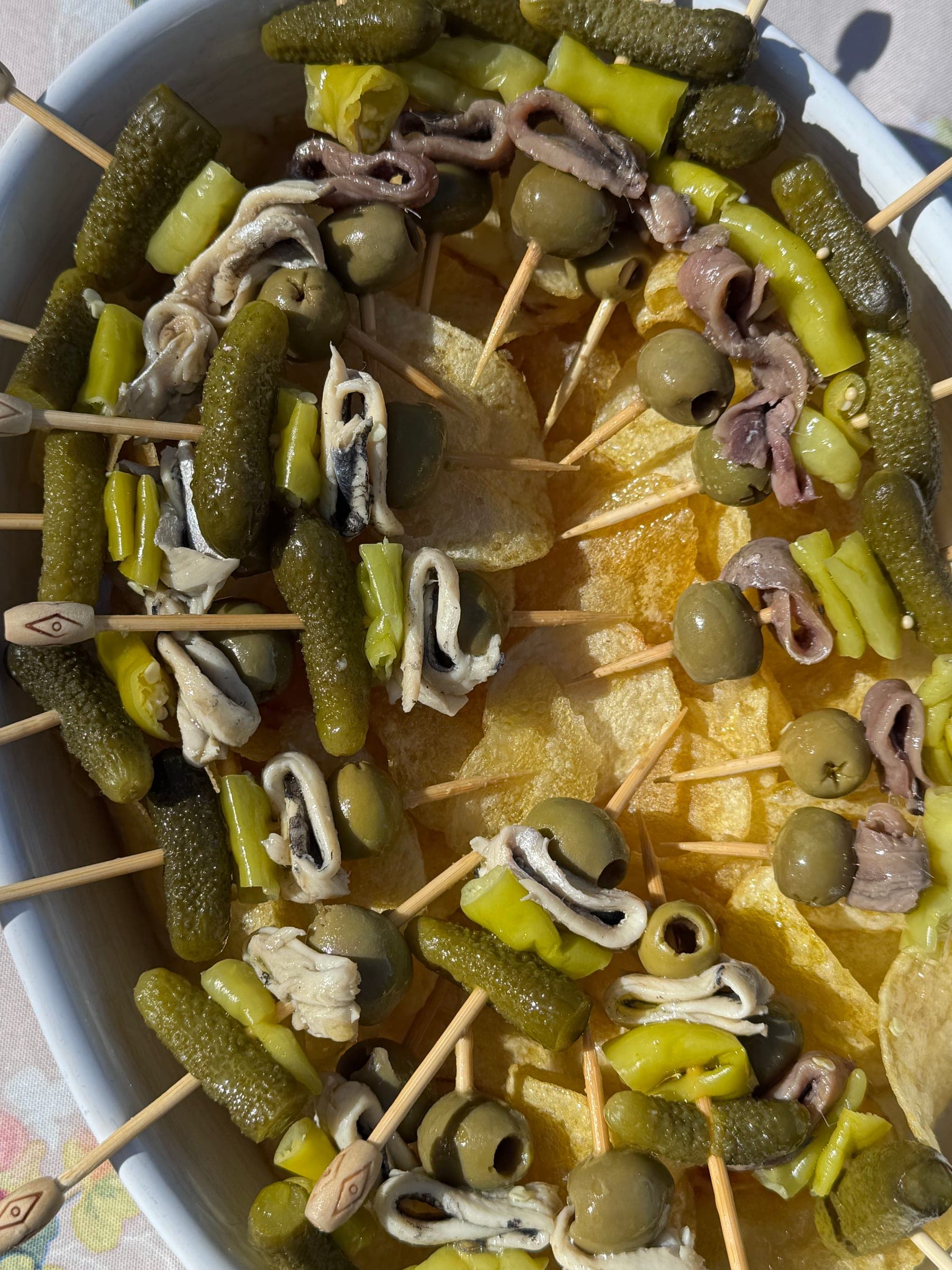 Weiße Schale mit spanischen Banderillas aus Gurken, Oliven, Paprika und Anchovis auf Kartoffelchips